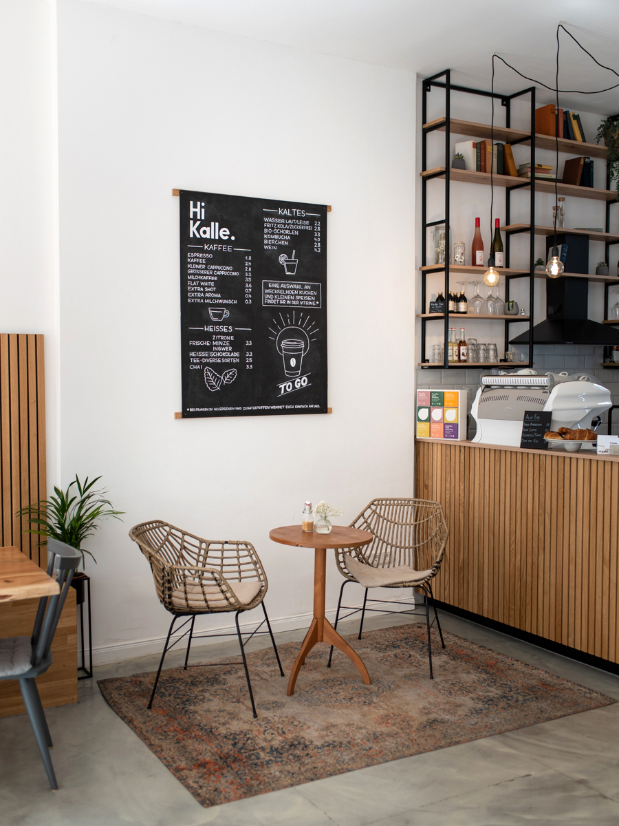 Innenaufnahme des Cafés Hi Kalle in Bochum mit hellen Holzmöbeln, Kaffeetheke und gemütlicher Sitzecke mit Teppich und Rattanstühlen.