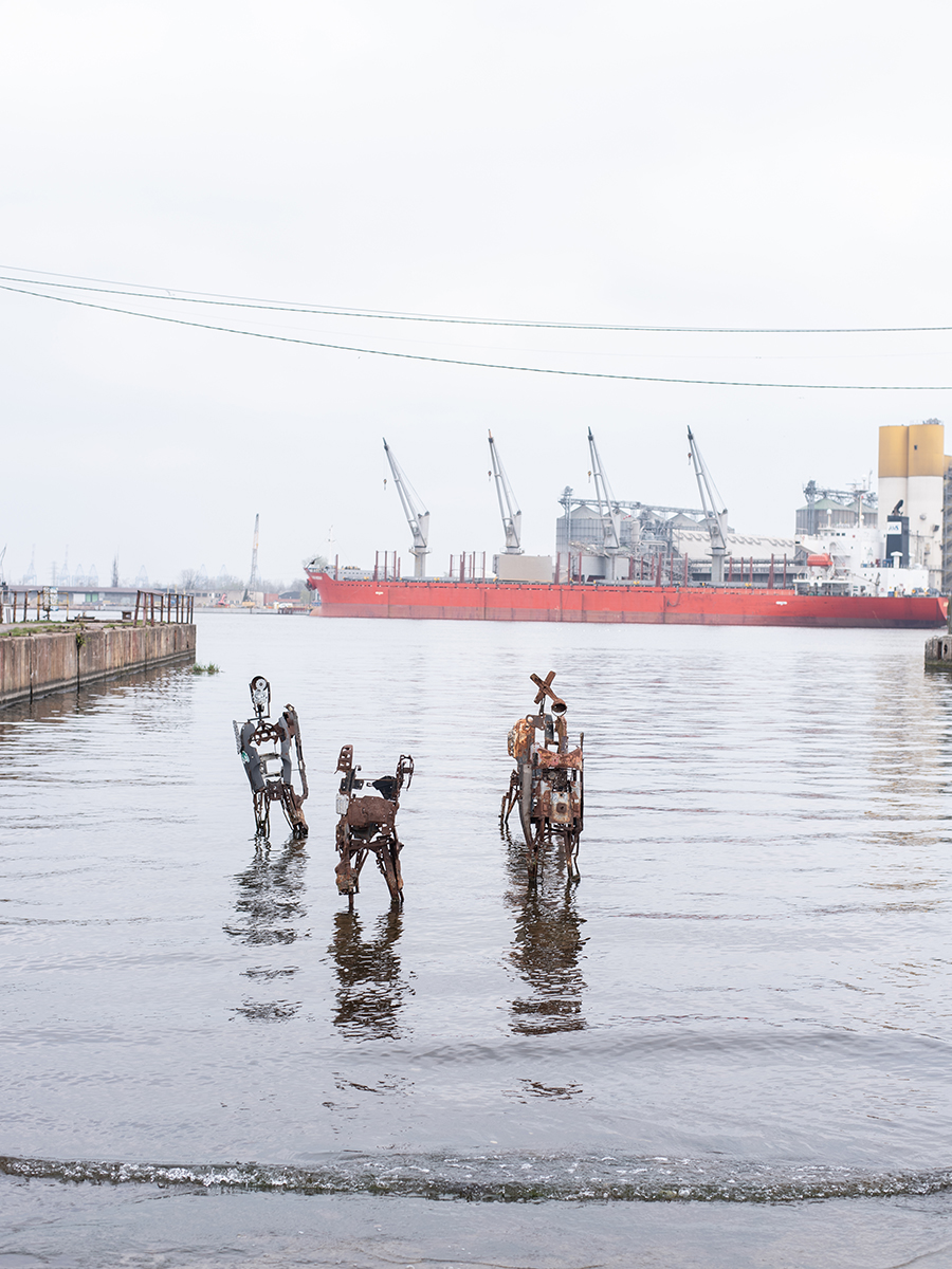 Metallskulpturen im Wasser des Danziger Hafens vor einem roten Frachtschiff