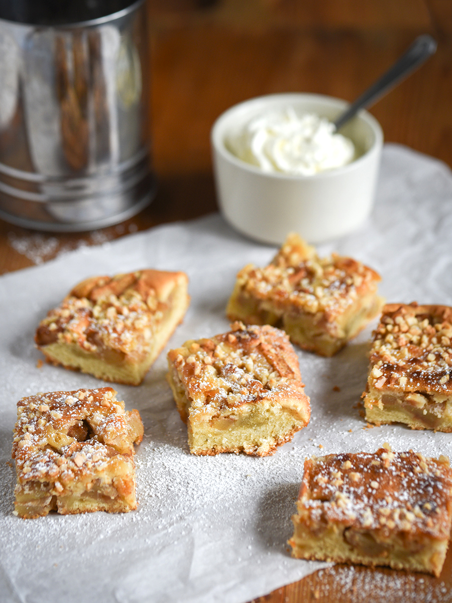 Saftige Stücke Apfelkuchen vom Blech mit Marzipan und gehackten Mandeln auf Backpapier