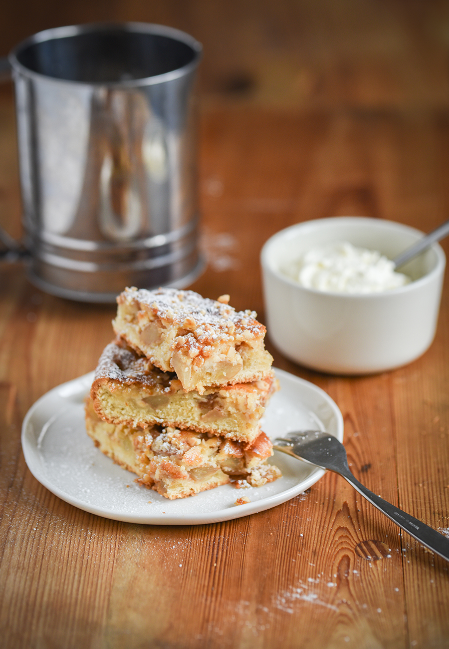 Stücke Apfelkuchen mit Marzipan auf einem Teller, bestäubt mit Puderzucker