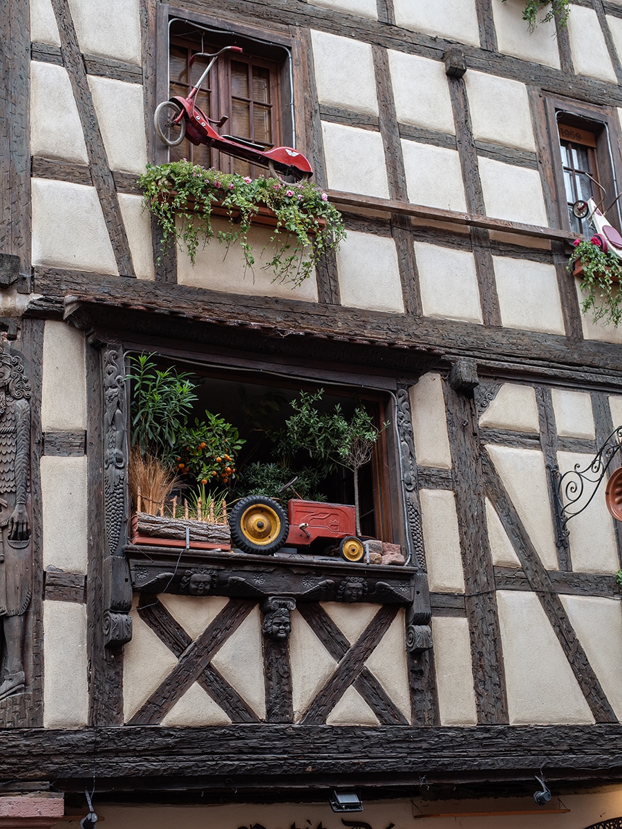 Fachwerkfassade mit alter Spielzeug-Deko in den Fenstern in Riquewihr