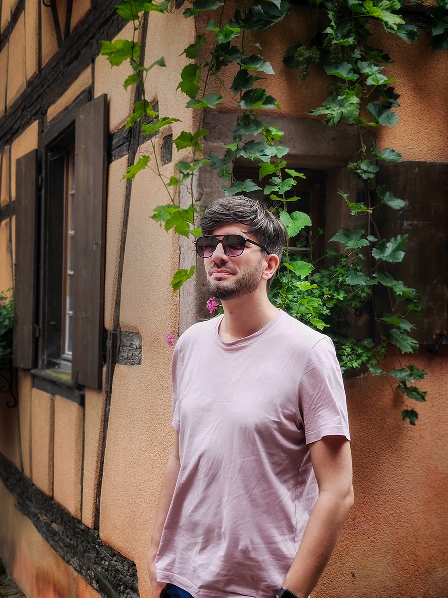 Menschen spazieren durch die Altstadt von Riquewihr mit bunten Fachwerkhäusern
