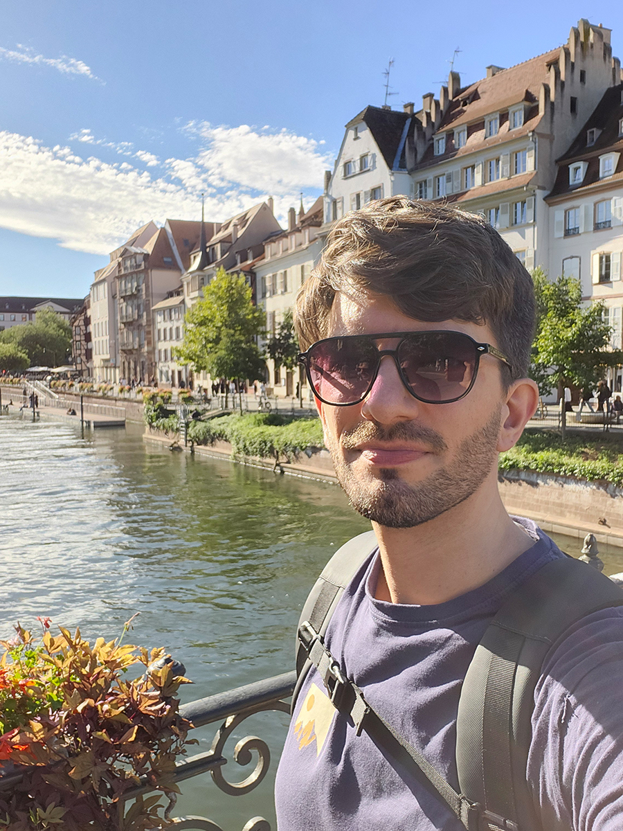 Person mit Sonnenbrille macht ein Selfie am Fluss in Straßburg, im Hintergrund Altstadthäuser