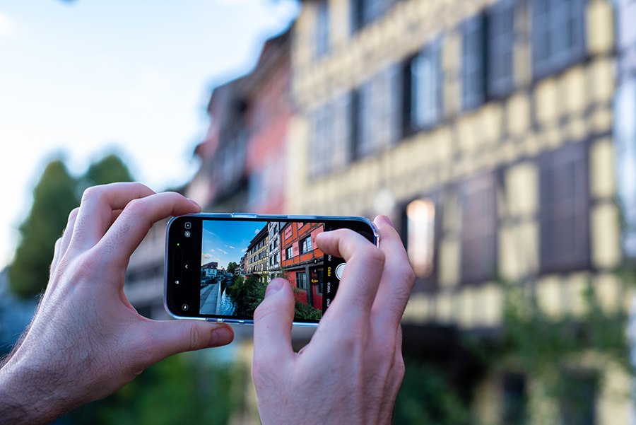 Hände halten ein Smartphone, das Straßburgs Fachwerkhäuser und Fluss zeigt