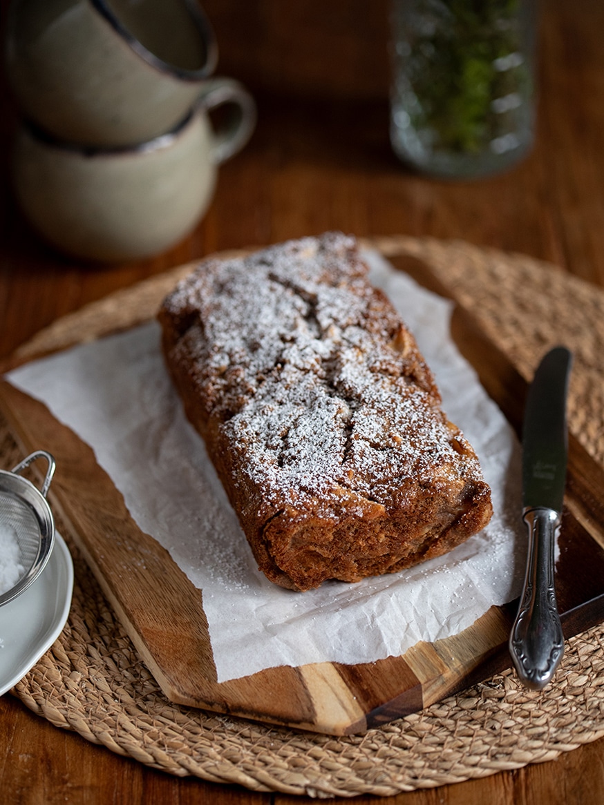 Kleiner Apfel-Mandel-Kuchen in der Kastenform, bestäubt mit Puderzucker, auf einem Holztisch serviert.