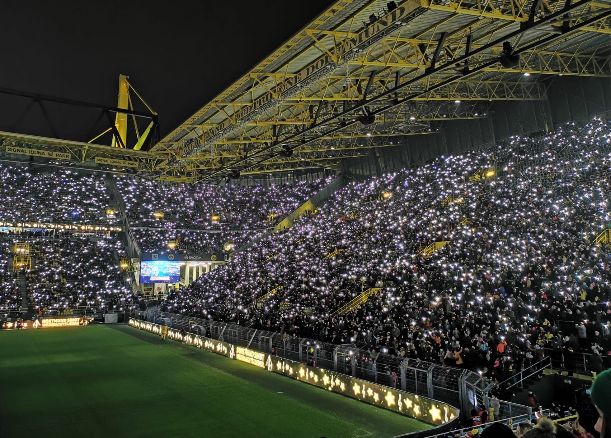 Flutlichtspiel im ausverkauften Fußballstadion in Dortmund mit leuchtenden Handylichtern der Fans