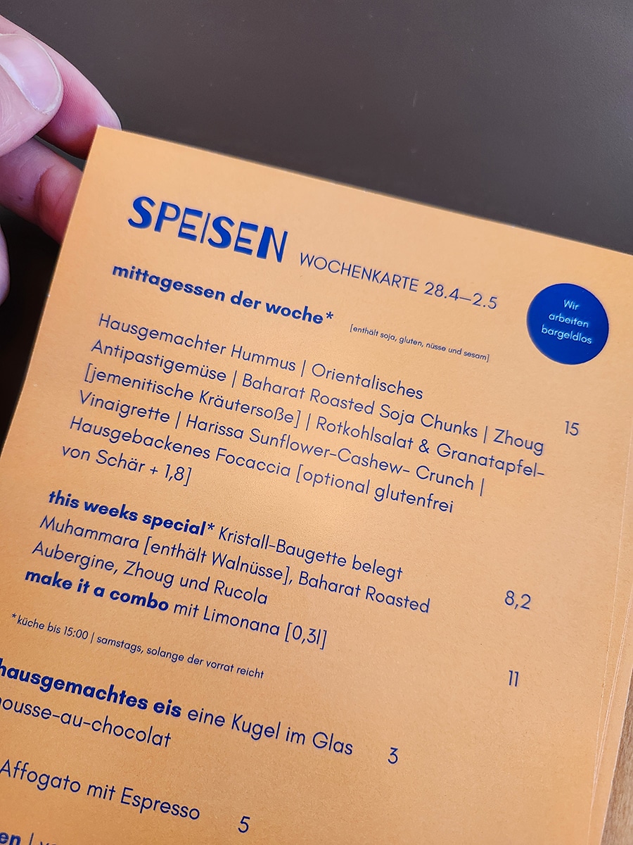 Speisekarte des Heinrichs in Paderborn mit veganen Gerichten und Getränken auf orangefarbenem Klemmbrett