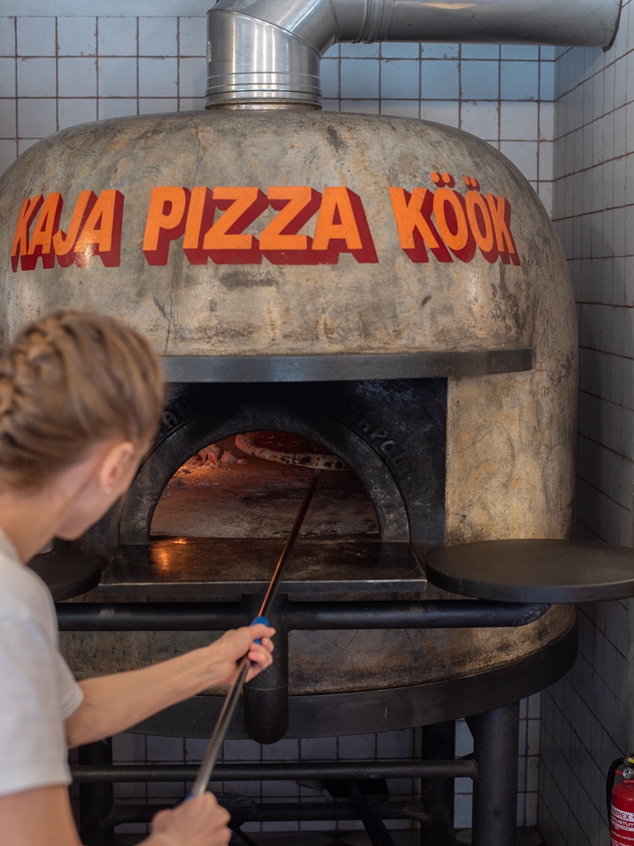 Mitarbeiterin schiebt eine Pizza in den Holzofen des Kaja Pizza Köök in Tallinn