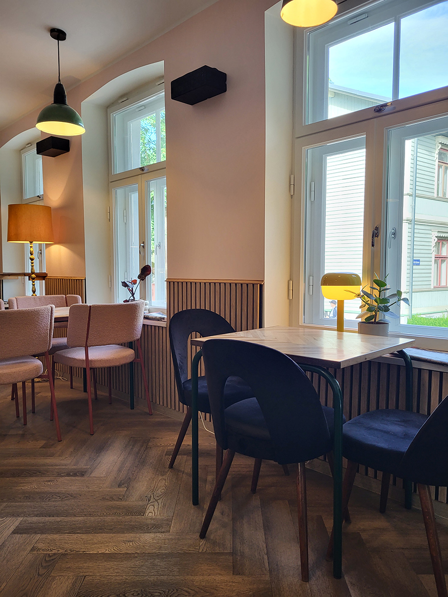 Innenraum des Kiosk No. 4 in Tallinn mit dunklen Stühlen, Holztischen und großen Fenstern
