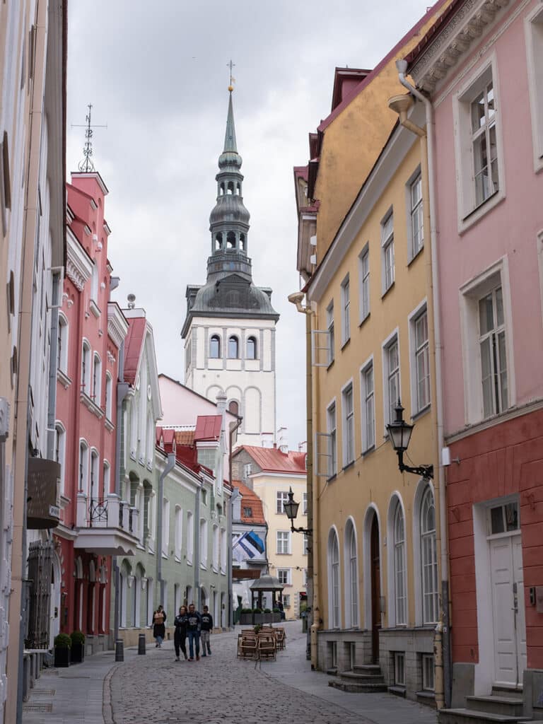 Straße in der Altstadt von Tallinn mit pastellfarbenen Häusern und einem Kirchturm im Hintergrund
