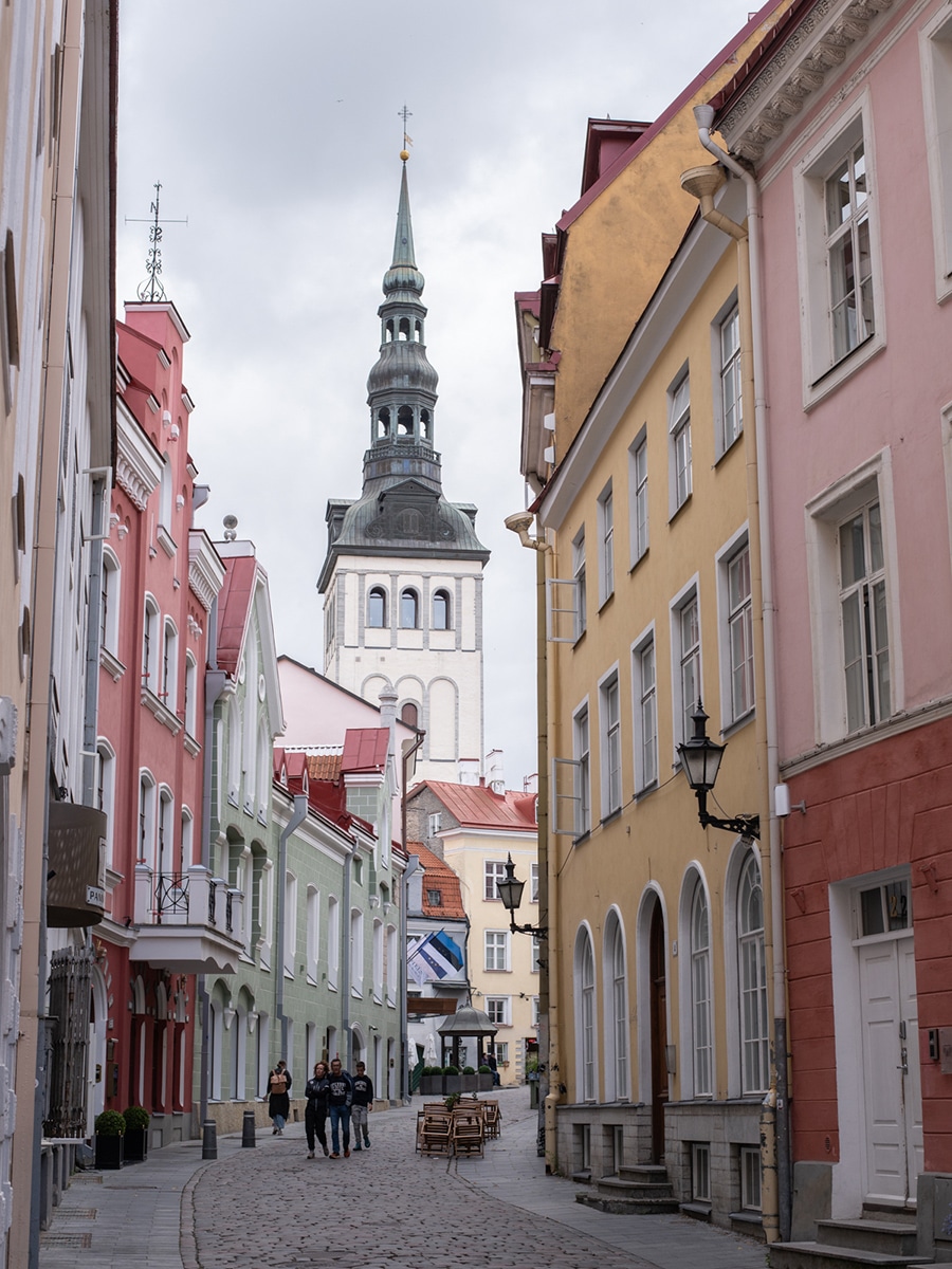 Straße in der Altstadt von Tallinn mit pastellfarbenen Häusern und einem Kirchturm im Hintergrund
