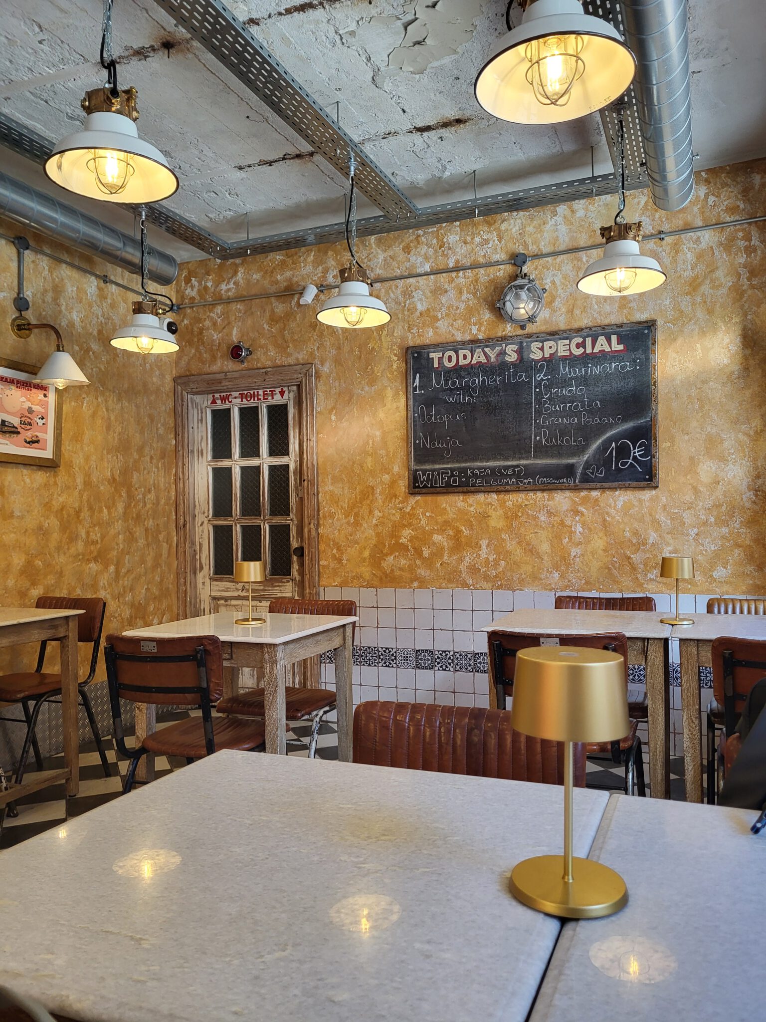 Innenraum des Kaja Pizza Köök in Tallinn mit Tischen, Stühlen und industrieller Einrichtung