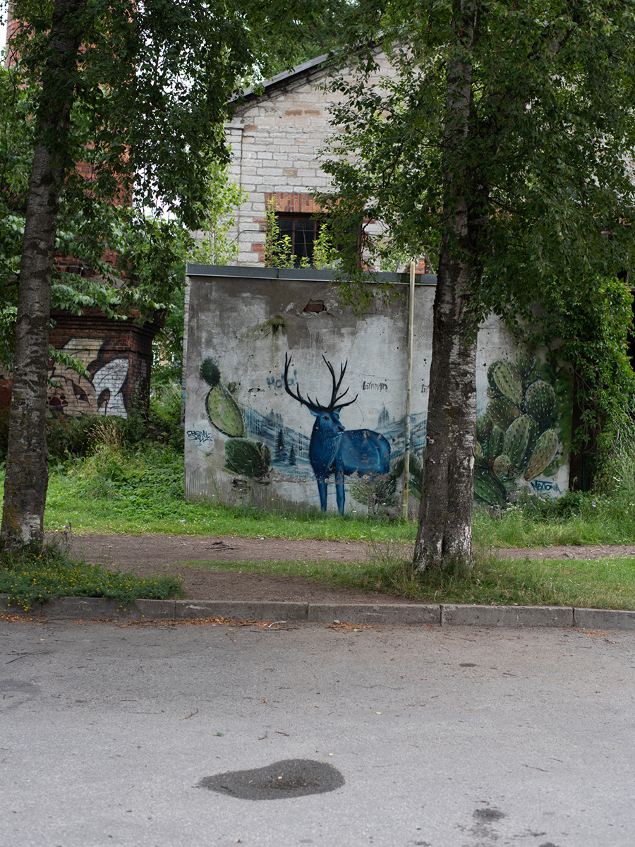 Mit Street-Art bemalter Stromkasten zwischen Bäumen in Telliskivi in Tallinn